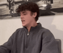 a young man with curly hair is sitting in a chair in front of a painting of an airplane .