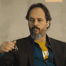 a man with a beard is holding a glass and wearing a shirt with the letter e on it