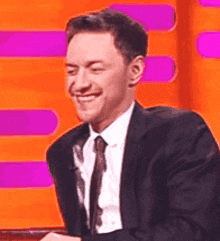 a man in a suit and tie is smiling in front of a pink and orange background .