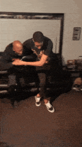 two men are dancing in a living room and one of them is wearing a shirt that says ' a ' on it
