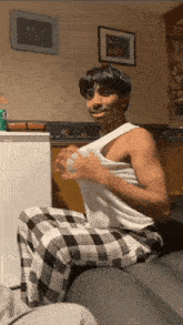 a man wearing plaid pants and a white tank top sits on a couch