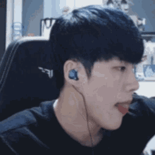 a young man with blue hair is wearing headphones and sticking his tongue out while sitting in a chair .