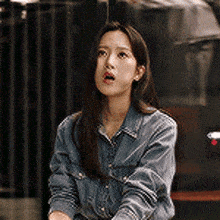 a woman in a denim shirt is sitting in a chair and looking at the camera .