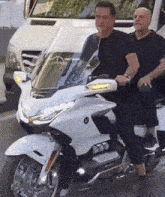 two men are riding a white motorcycle on a city street