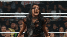 a woman is standing in a wrestling ring with a crowd behind her .