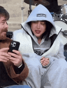 a man is holding a cell phone next to a woman wearing a hooded jacket .