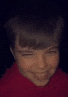a close up of a young boy 's face with a red shirt on .