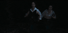 a couple standing in a dark room with leaves on the floor