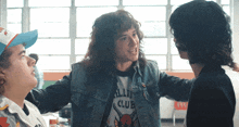 a man wearing a valley club t-shirt talks to another man