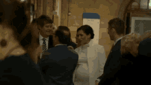 a pregnant woman in a white dress is talking to a group of people in a hallway .