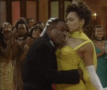 a man in a suit is kissing a woman in a yellow dress at a party .