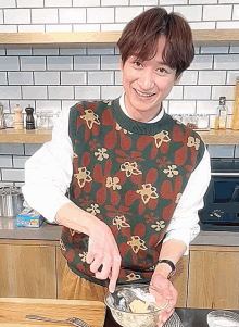 a man wearing a sweater with flowers on it is mixing ingredients in a bowl