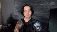 a man wearing a black jacket with a silver sleeve is talking to someone .