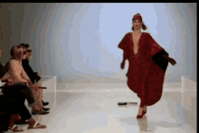 a woman is walking down a runway wearing a red dress and a hat .