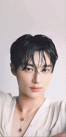 a young man wearing a white shirt and a necklace looks at the camera