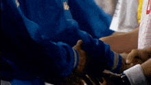 a group of people in blue jackets are shaking hands in a huddle .