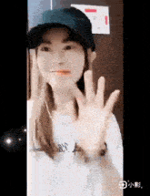 a woman wearing a baseball cap and a white shirt is waving at the camera .