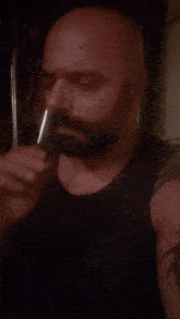 a bald man with a beard is wearing a black tank top and has a tattoo on his arm