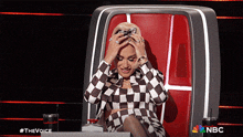 a woman in a black and white checkered dress is sitting in a chair with her hands on her head