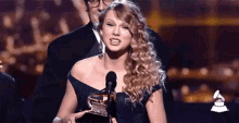 a woman in a blue dress is holding a grammy award on a stage .