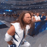 a man with long hair and a beard is standing in front of a crowd wearing a white vest