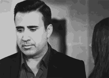 a black and white photo of a man in a suit and a woman looking at him .