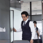 a man in a vest and tie stands in front of a glass door