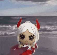 a doll with white hair and red horns is on the beach