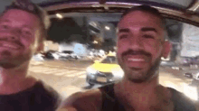 two men are sitting in the back seat of a car and smiling at the camera .