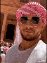 a man wearing sunglasses and a head scarf with arabic writing on the bottom