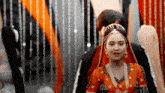 a man and a woman are standing next to each other in a room . the woman is wearing an orange dress .