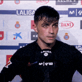 a man wearing a black laliga shirt stands in front of a wall with laliga and dani logos