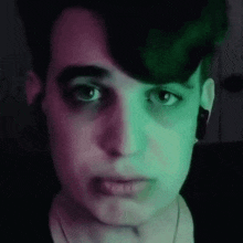 a close up of a person 's face with a purple and green light behind it .