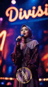 a woman in a hijab singing into a microphone in front of a sign that says divisi