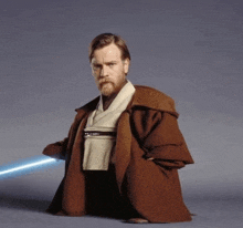 a man with a beard wearing a brown coat holds a light saber