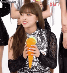 a girl in a sequined top is holding an orange carrot