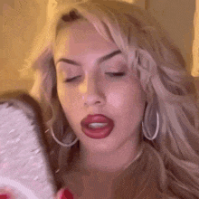 a woman is looking at herself in a mirror while wearing red lipstick and hoop earrings .