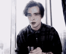 a young man in a plaid shirt holds a microphone