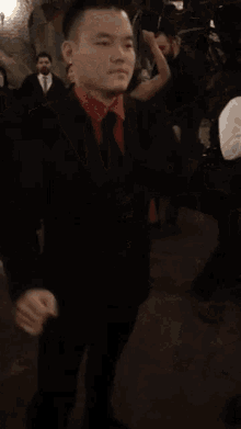 a man in a black suit and red shirt is dancing in a crowd