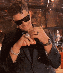 a man wearing sunglasses and a ring on his finger looks at his watch