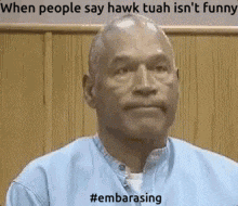a man in a blue shirt is sitting in front of a wooden wall and says when people say hawk tuah