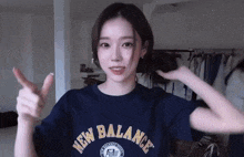 a woman wearing a blue new balance shirt is giving a thumbs up .