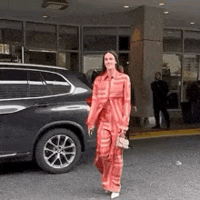 a woman in a red suit is walking in front of a bmw x5 .