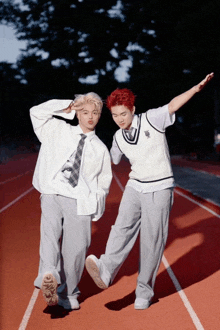 two young men standing on a track with their arms outstretched and one has red hair