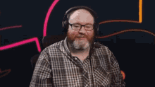 a man with a beard and glasses wearing headphones and a plaid shirt .