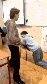 a man kneeling down in a classroom with another man standing behind him