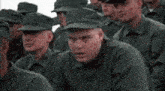 a man in a military uniform is sitting in a crowd of soldiers and looking at the camera .