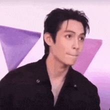 a man in a black jacket is making a funny face in front of a purple background .