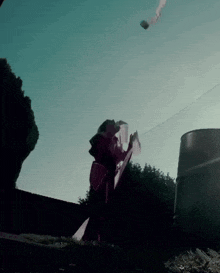 a person standing in front of a fence looking up at a kite