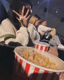 a striped bucket of popcorn sits in front of a woman sitting in a theater